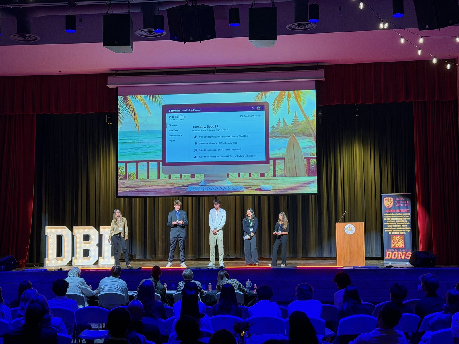 The winning team of five on stage presenting the WAVES trip-planner mockup to a full audience.