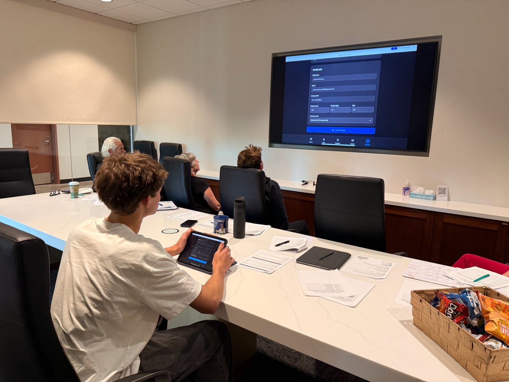 A student demos the DietLabs app from an iPad while it mirrors onto the boardroom screen for the interview panel.